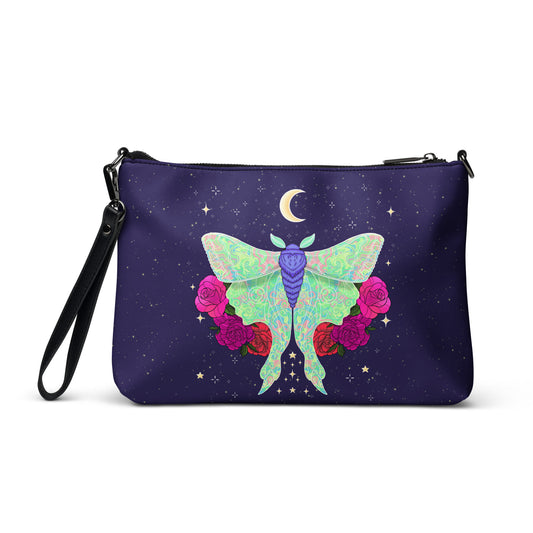 A dark purple wristlet clutch bag featuring a whimsical graphic of a green patterned moth, pink roses, a crescent moon, and small stars on a white background.