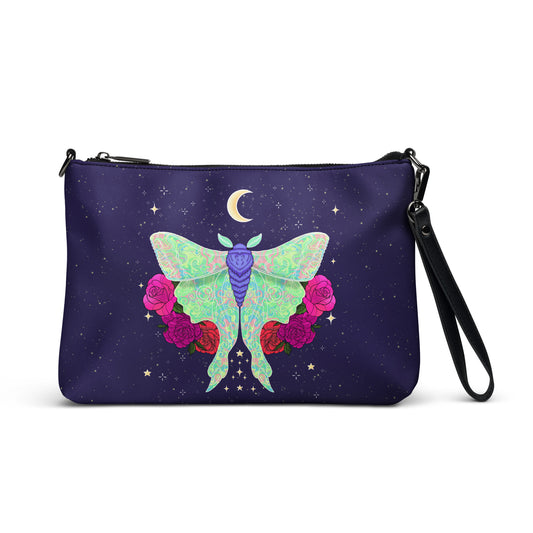 A navy blue wristlet clutch bag featuring a colorful celestial print with a large green and purple moth, pink roses, stars, and a crescent moon, shown on a plain white background.