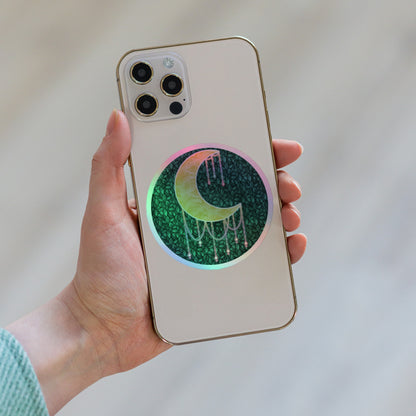 Druzy Moon holographic sticker 4x4 inch – hand-drawn crescent moon with jewel drips on a dark leafy background, rainbow holographic border, by Brittyliz Art